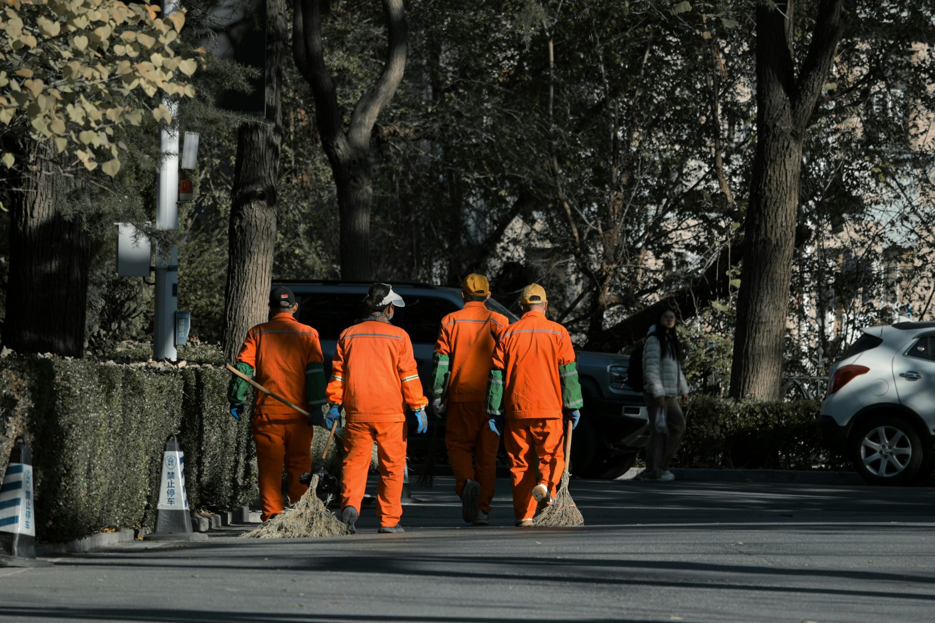 Four sanitation workers in orange uniforms with brooms